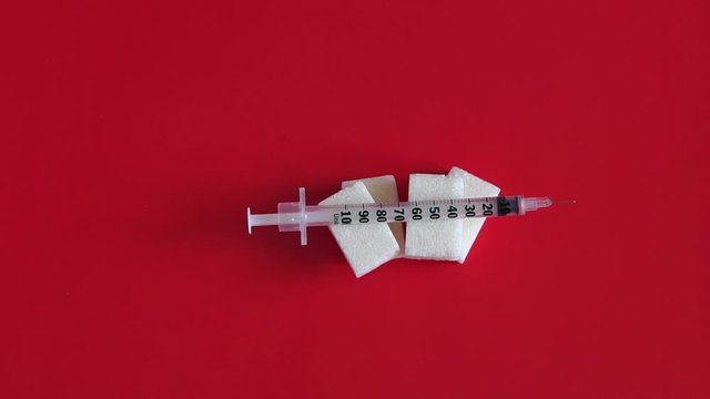 Close-up of insulin syringe lying on the cubes of refined sugar on a red background. Diabetes. Slow motion. Health care and diabetes healing concept. Health care and diabetes healing concept.