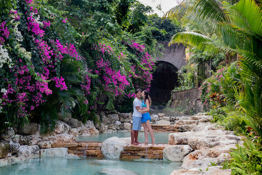 Kissing couple in love. Multiracial couple hugging. Multiethnic couple at the swimming pool. Swimming pool surrounded by pink bougainvillea flowers.