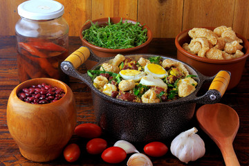Feijao Tropeiro typical dish of Brazilian cuisine, made with beans, bacon, sausage, collard greens, eggs, on rustic wooden table.