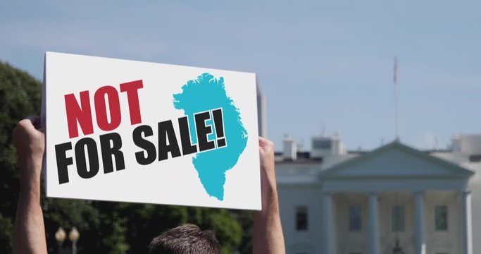 A man holds a GREENLAND NOT FOR SALE protest sign in front of the White House on a sunny summer day.	 	