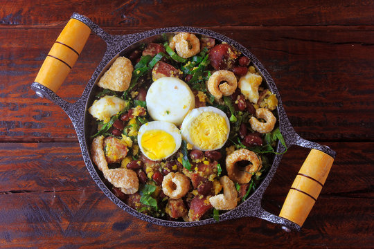 Feijao Tropeiro typical dish of Brazilian cuisine, made with beans, bacon, sausage, collard greens, eggs, on rustic wooden table.