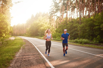 Caucasian female sports woman and fit man in full body length running pine forest road. healthy...