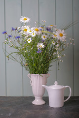 White teapot with tea and a bouquet of daisies and cornflowers in a