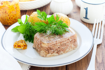 Homemade jelly chicken decorated with greens and eggs on plate on wooden background close up. Cold Meat Dishes. Top view