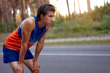 Jogging man taking a break during training outdoors on pine forest road.