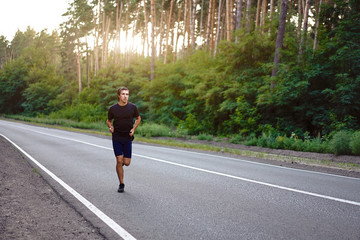 Caucasian middle age man athlete runs sunny summer day on asphalt road in the forest.