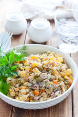 Russian traditional salad Olivier with vegetables and meat. Winter saladHomemade salad Olivier with boiled meat and meat on a wooden table, selective focus