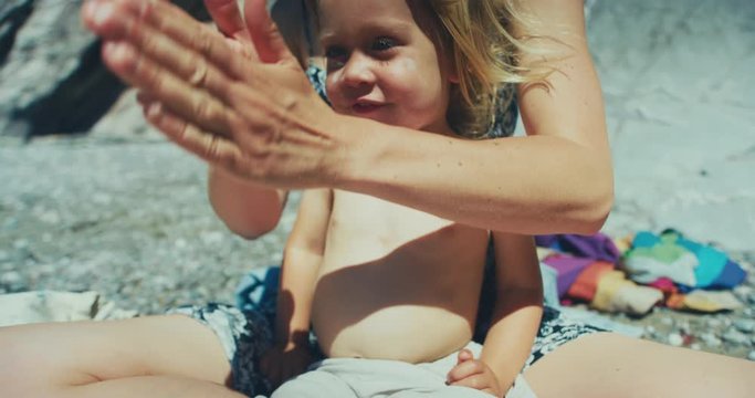 Young mother applying sun lotion to her toddler's body on the beach