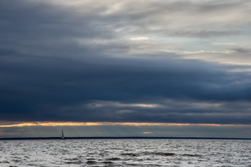Obraz premium Small yacht on the waves against the background of the gloomy sky. Sun rays through the clouds. Windy, the sea is worried. Sail on the horizon.