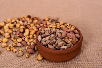 Almonds, pistachios, hazelnuts and round nuts in bowl on textured light brown background. Table view food.