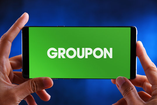 Hands holding smartphone displaying logo of Groupon