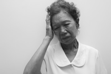 Elderly Asian woman holding her head, having a strong headache and fever. Black & white