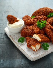 Breaded chicken strips with mayonnaise on white wooden board