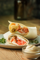 Fresh tortilla wrap with vegetables and salmon on plate