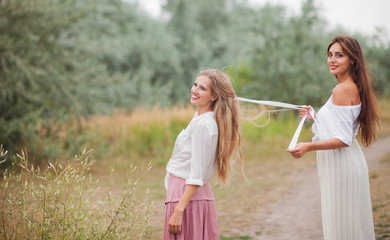 Two cheerful best girlfriends in retro-style clothes on landing with the road at summer day