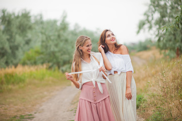 Fototapeta na wymiar Two cheerful emotional best girlfriends in retro style clothes in retro clothes walk along the landing with the road on summer cloudy day. Walk together