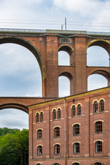 Fototapeta premium Mylau, Saxony, Germany. The building of the historic Ketzel flour mill is dwarfed by the arches of the Goeltzschtalbridge, the largest brick-built bridge in the world,