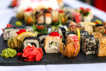 Set of sushi rolls with vasabi and ginger on a dark slate plate, Buffet table, horizontal orientation, close up