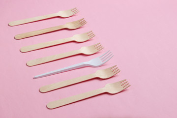 Minimalistic environmental concept. Wooden and plastic forks on a pink pastel background. Creative eco background