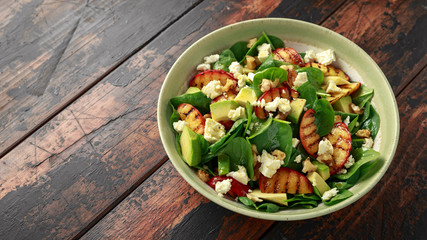 Summer Peach Salad with spinach, avocado, walnuts and feta cheese in rustic bowl. healthy food.