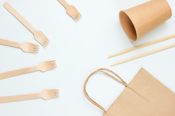 Disposable tablewar of natural materials. Eco friendly concept. Wooden forks, empty craft coffee cup, bag, chopsticks on a white background. Top view