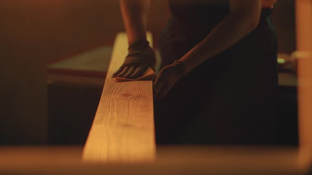 Close up of man`s hands grinding plank with sandpaper in workshop during the sunset. Woodworking, carpentering, craft, profession concept.