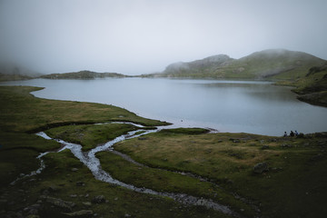 Fototapeta premium Three friends having a conversation in a high altitude lake in the mountain on a dark foggy day