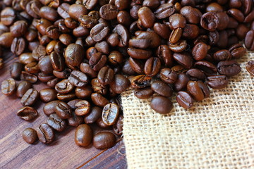 close up coffee beans on sack with brown wood background.roasted coffee beans high quility from organic farm .