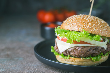 Hamburger with beef meat burger and fresh vegetables on dark background. Tasty fast food.