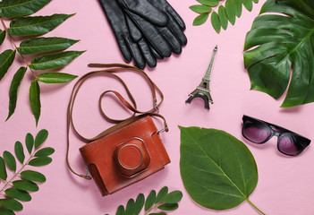 Jorney to Paris. Women's accessories, retro camera, figurine of the Eiffel tower on pink pastel background with green leaves. Top view