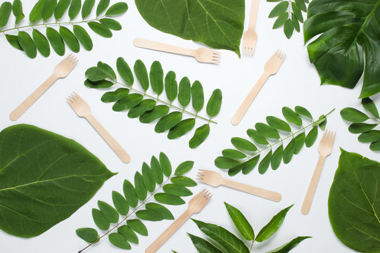 Many wooden forks among green tropical leaves on a white background. Creative eco background