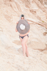 Young beautiful Caucasian woman in striped big hat with fashion swimwear posing in desert landscape...