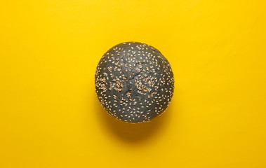 Black bun with sesame seeds on yellow background. Top view