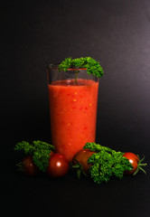 Still life. Tomato juice in a glass cup, cherry tomatoes and green leaves of parsley on a black background. close-up. Isolated, Vegetarianism.