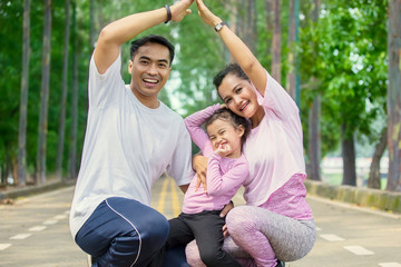 Fototapeta premium Cheerful family making house symbol in the park