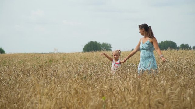 Little Girl with Mother Walking Through the Golden Wheat Field in Autumn Day. Concept of Freedom, Harvest, Recreation and Agriculture