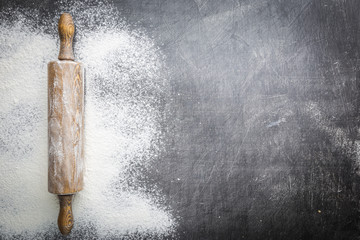 Rolling pin and white flour on a dark background. Free space for text . Top view.