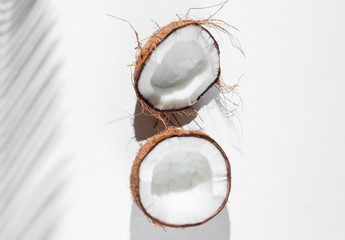 Minimalistic tropical still life. Halves coconut with shadows from palm leaves on white background. Creative fashion concept. Top view.