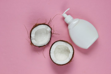 Two halves of chopped coconut and white bottle of cream on pink background. Creative fashion concept. Top view