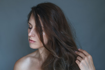 Portrait of a young woman touching her fluffy dark chocolate brown hair with her hand