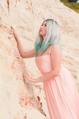 Young beautiful Caucasian woman in long pink dress posing in desert landscape with sand.