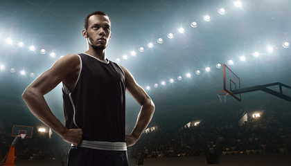 Young african-american basketball player in sports uniform on empty floodlit basketball court with the ball