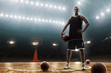 Young african-american basketball player in sports uniform on empty floodlit basketball court with...