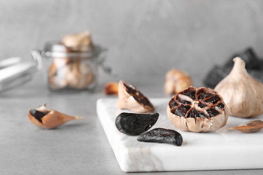 Marble board with black garlic on grey table. Space for text