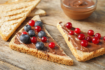 Slices of bread with chocolate paste and berries on wooden table