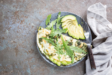 Omelette with avocado and arugula on gray ceramic plate on stone background, top view. Healthy breakfast.