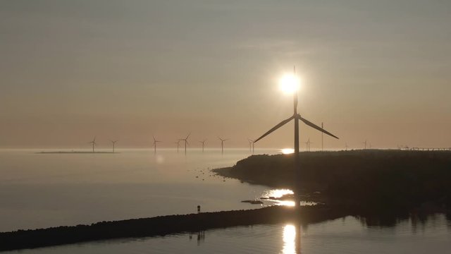 Sunset and windmills. Golden sky and horizon. Rotating mills. Drone shot of landscape with sea. Reflection in the water.
