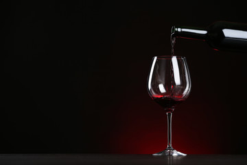 Pouring wine from bottle into glass on table against dark background, space for text