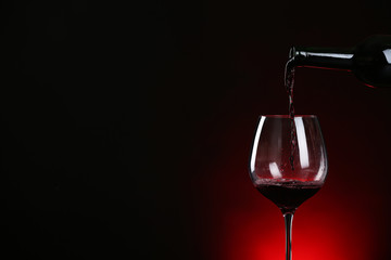 Pouring wine from bottle into glass on dark background, space for text