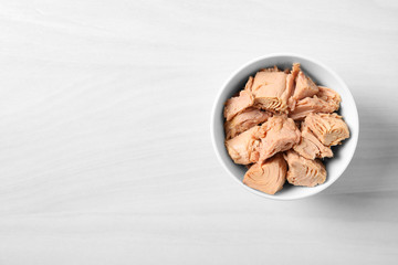 Bowl with canned tuna on light table, top view. Space for text
